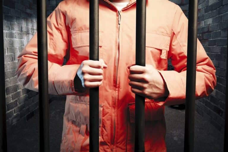 Image is of a man wearing an orange jumpsuit behind prison bars, concept of "What is the criminal defense process in Tennessee'?