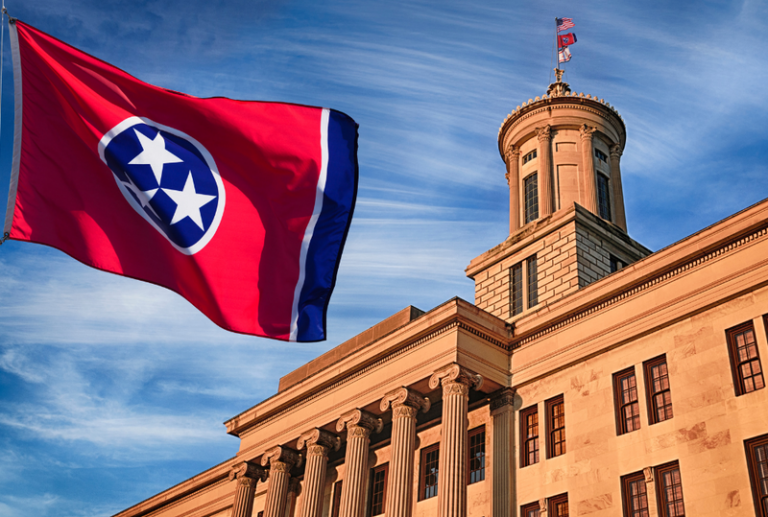 Image is of the Tennessee state capitol building with a Tennessee flag blowing in the wind, concept of new immigration law in Tennessee